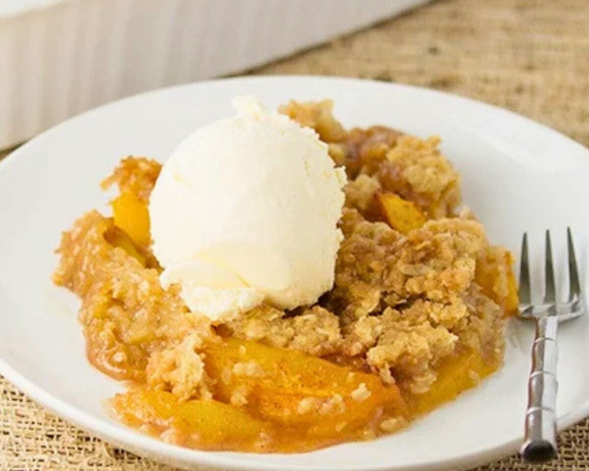 fresh peach crisp served on a white plate with a scoop of vanilla ice cream.