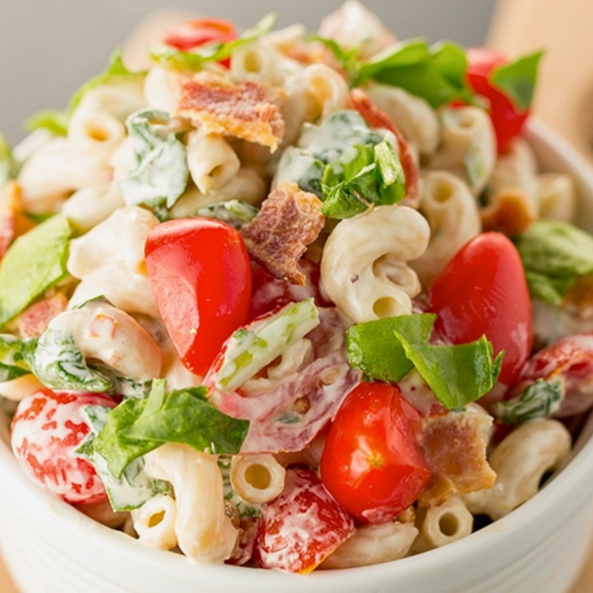 BLT pasta salad with bacon, cherry tomatoes, spinach and creamy dressing in a bowl.