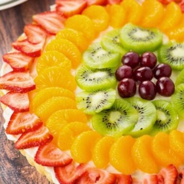 close-up of colorful fruit pizza made with a sugar cookie crust, cream cheese frosting and topped with fresh fruit: strawberries, oranges, kiwi and grapes.