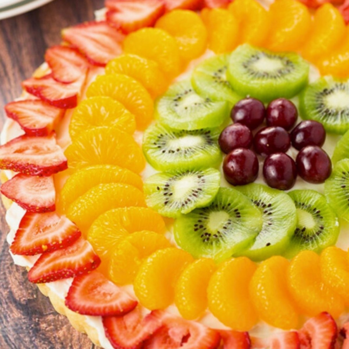 close-up of colorful fruit pizza made with a sugar cookie crust, cream cheese frosting and topped with fresh fruit: strawberries, oranges, kiwi and grapes.