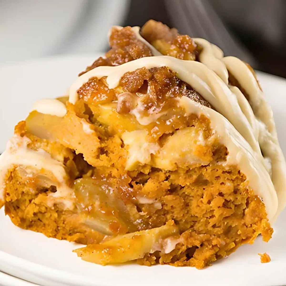 pumpkin apple spice Bundt Cake topped with cream cheese glaze on a white plate.