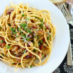 a bowl of creamy bucatini carbonara garnished with freshly chopped parsley and grated cheese.
