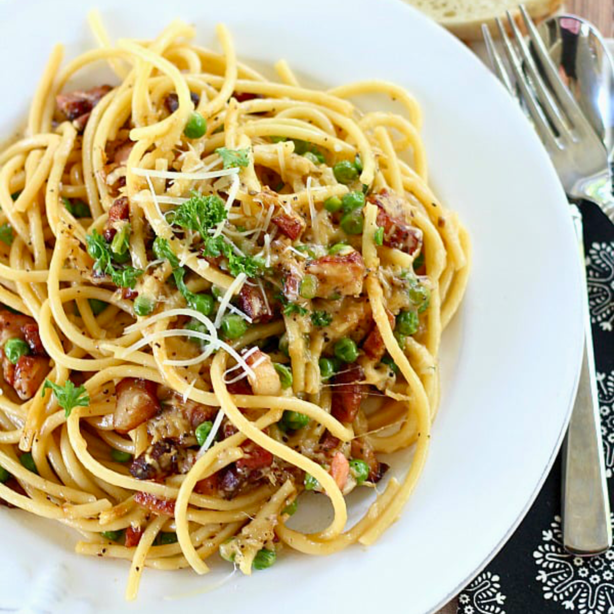 a bowl of creamy bucatini carbonara garnished with freshly chopped parsley and grated cheese.