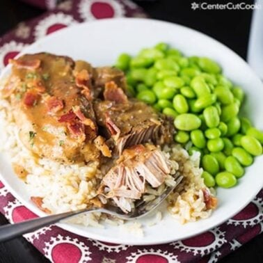 plate of slow cooker smothered pork chops over rice with a side of green vegetable