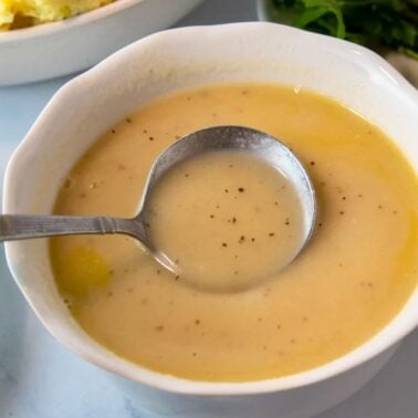 homemade turkey gravy in a small bowl with a lady,, perfect for thanksgiving dinner.