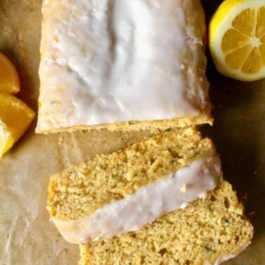 moist lemon zucchini bread with glaze drizzled on top, sliced on a cutting board.