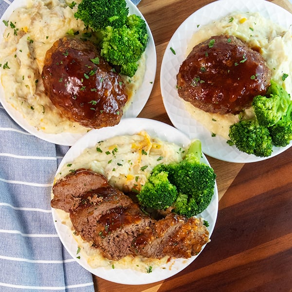 individual BBQ cheddar meatloaf sliced on a plate served with mashed potatoes and broccoli.