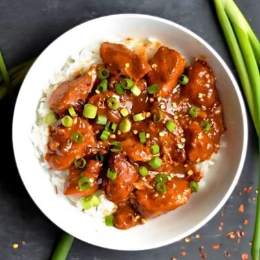 bowl of slow cooker general Tso's chicken served over white rice and garnished with green onions.