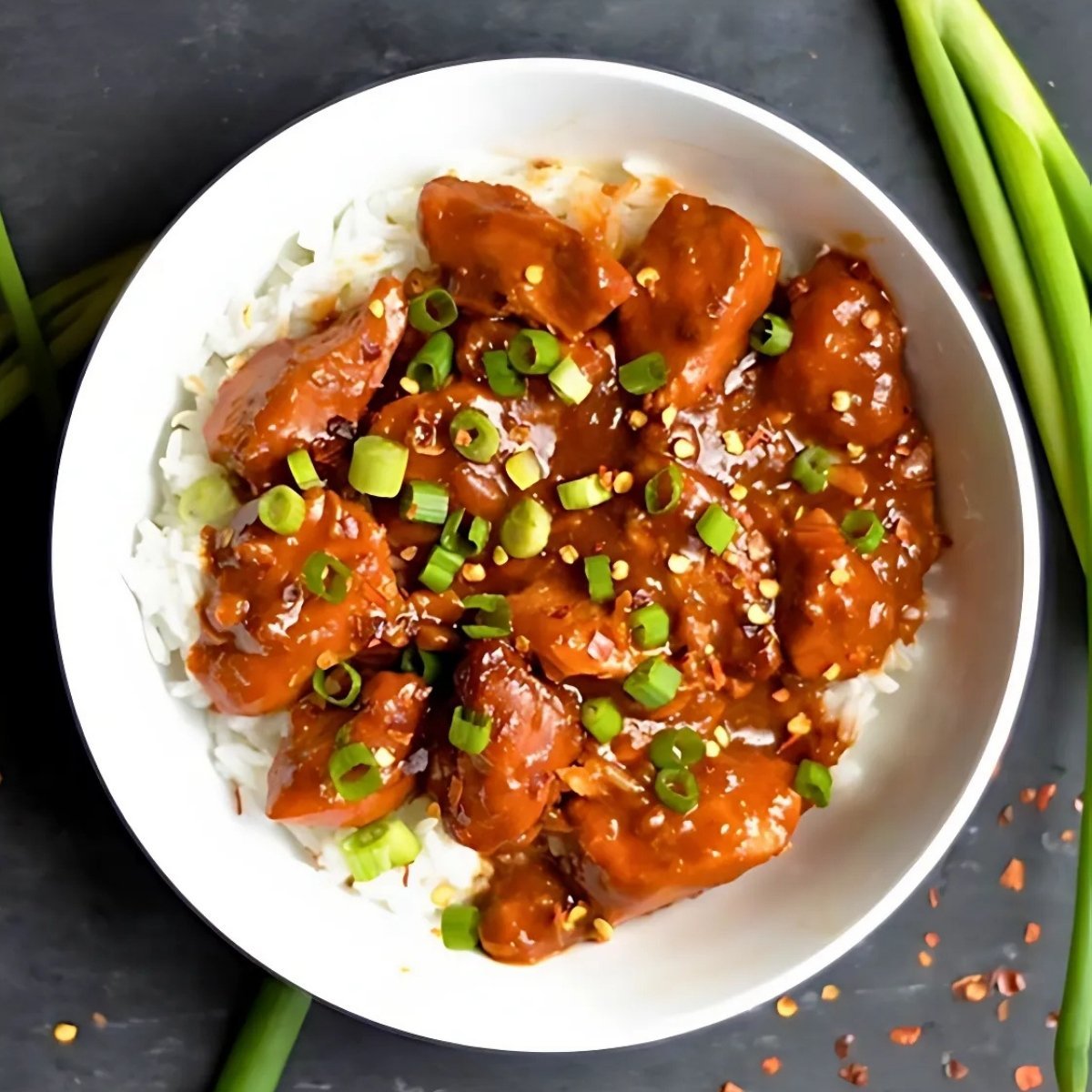 bowl of slow cooker general Tso's chicken served over white rice and garnished with green onions.