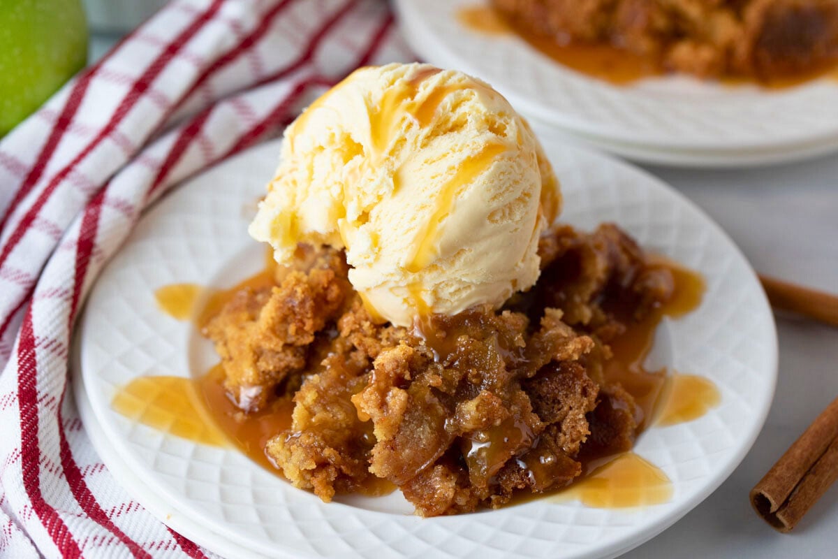 piece of caramel apple dump cake on a plate with ice cream and caramel sauce.