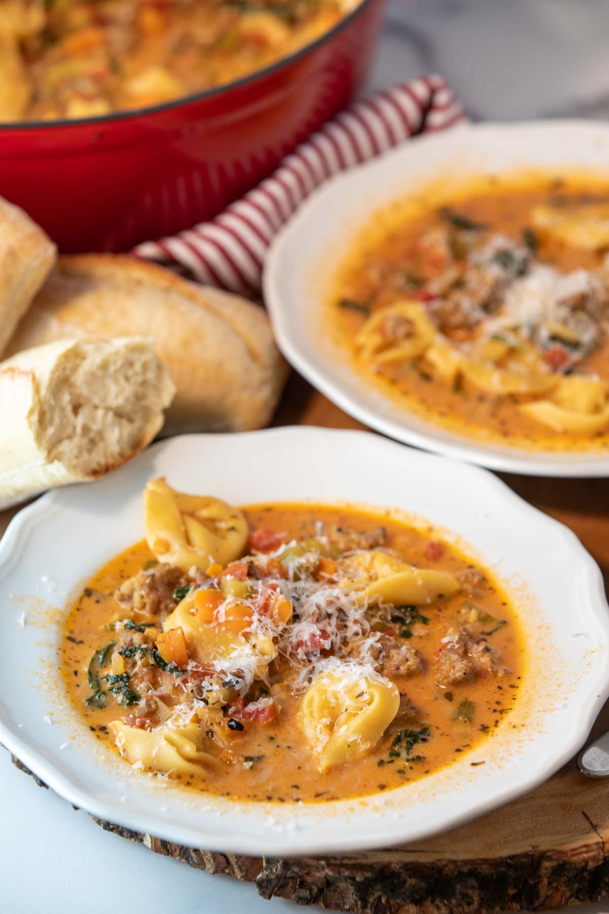 two bowls of spicy tortellini soup with bread and spoons sitting beside