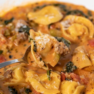 Bowl of spicy tortellini soup with a spoon.