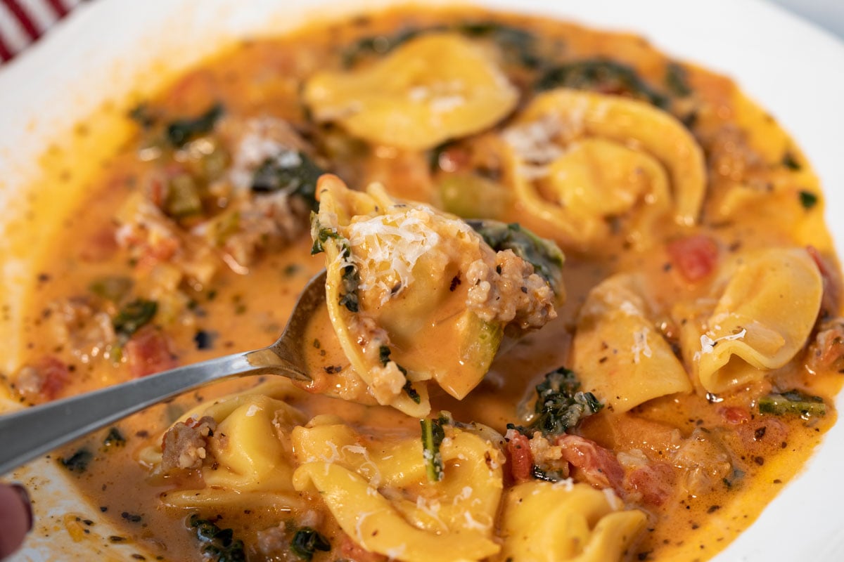 Bowl of spicy tortellini soup with a spoon.