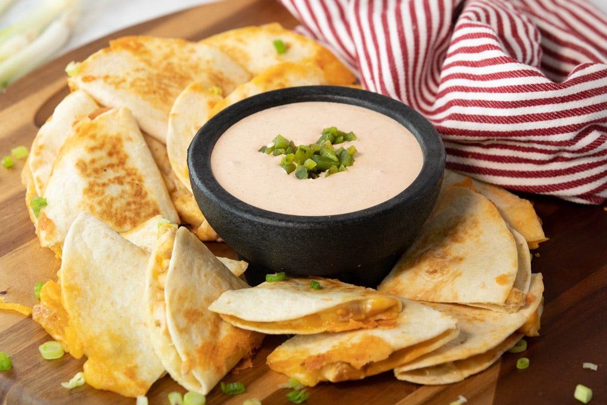 bowl of taco bell quesadilla sauce surrounded by a cut up a quesadilla