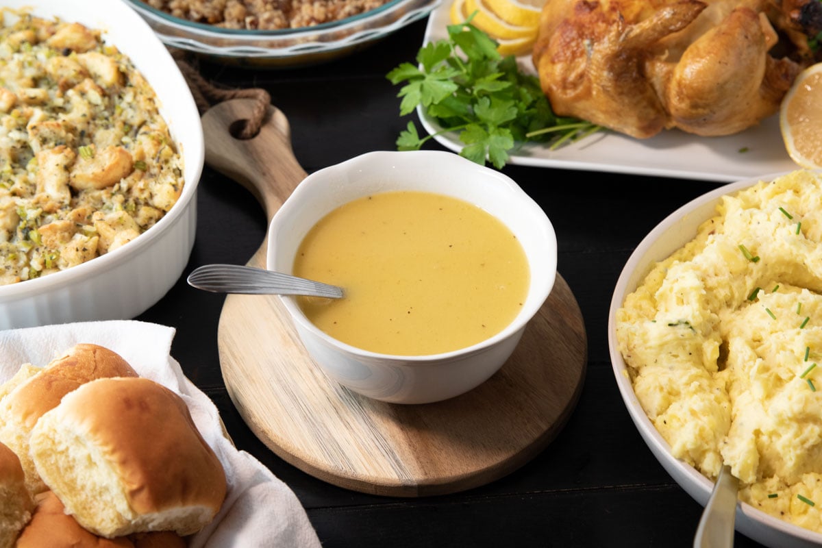bowl of perfect turkey gravy with a ladle surrounded by other Thanksgiving dishes