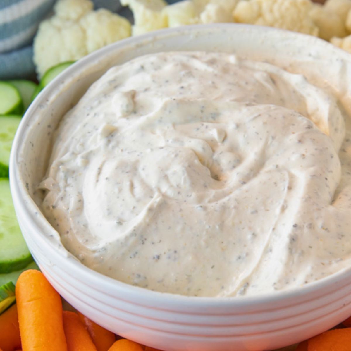 the best ranch dip recipe in a white bowl surrounded by carrots, cucumber, and cauliflower