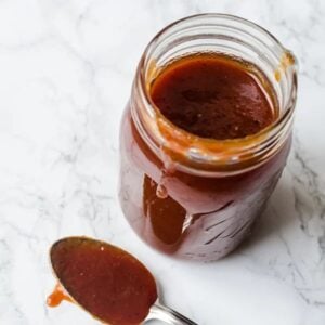 jar of homemade Barbecue Sauce with a spoon beside.