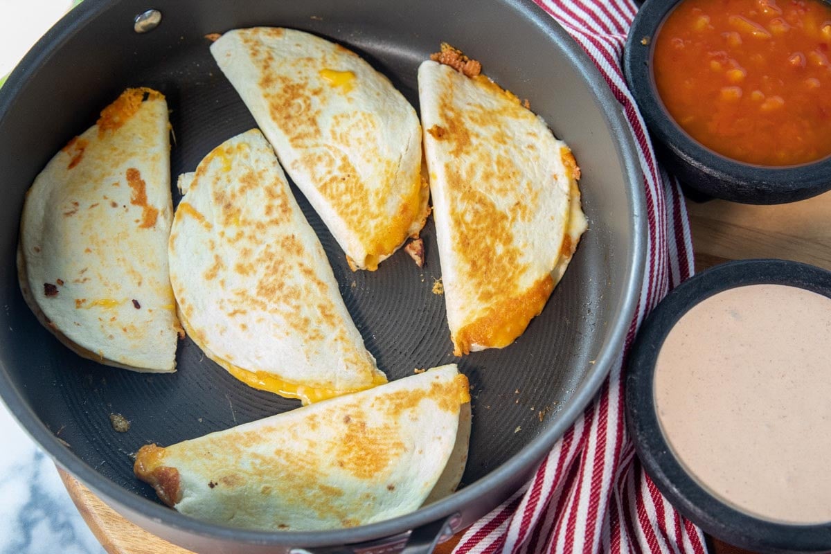 quesadillas in pan. Bowls of salsa and queso sitting beside for serving