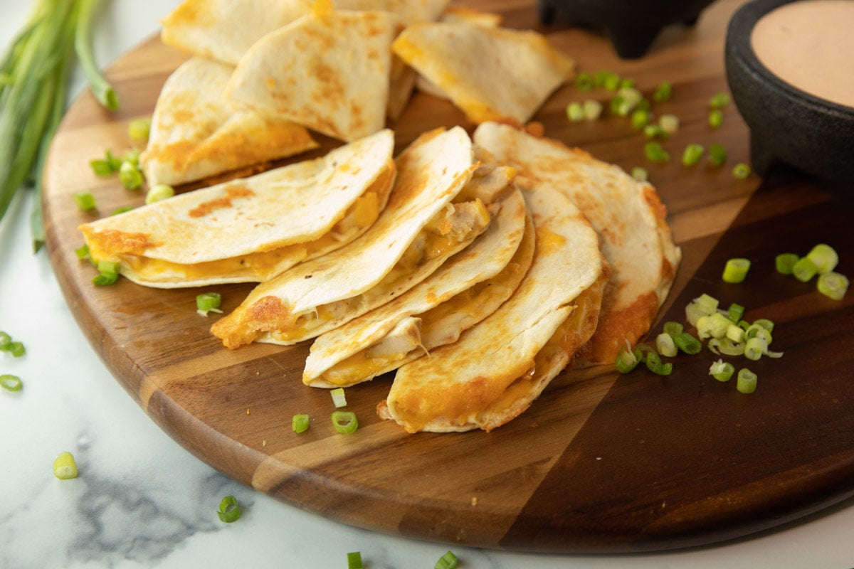 quesadillas on a serving board with bowl of queso