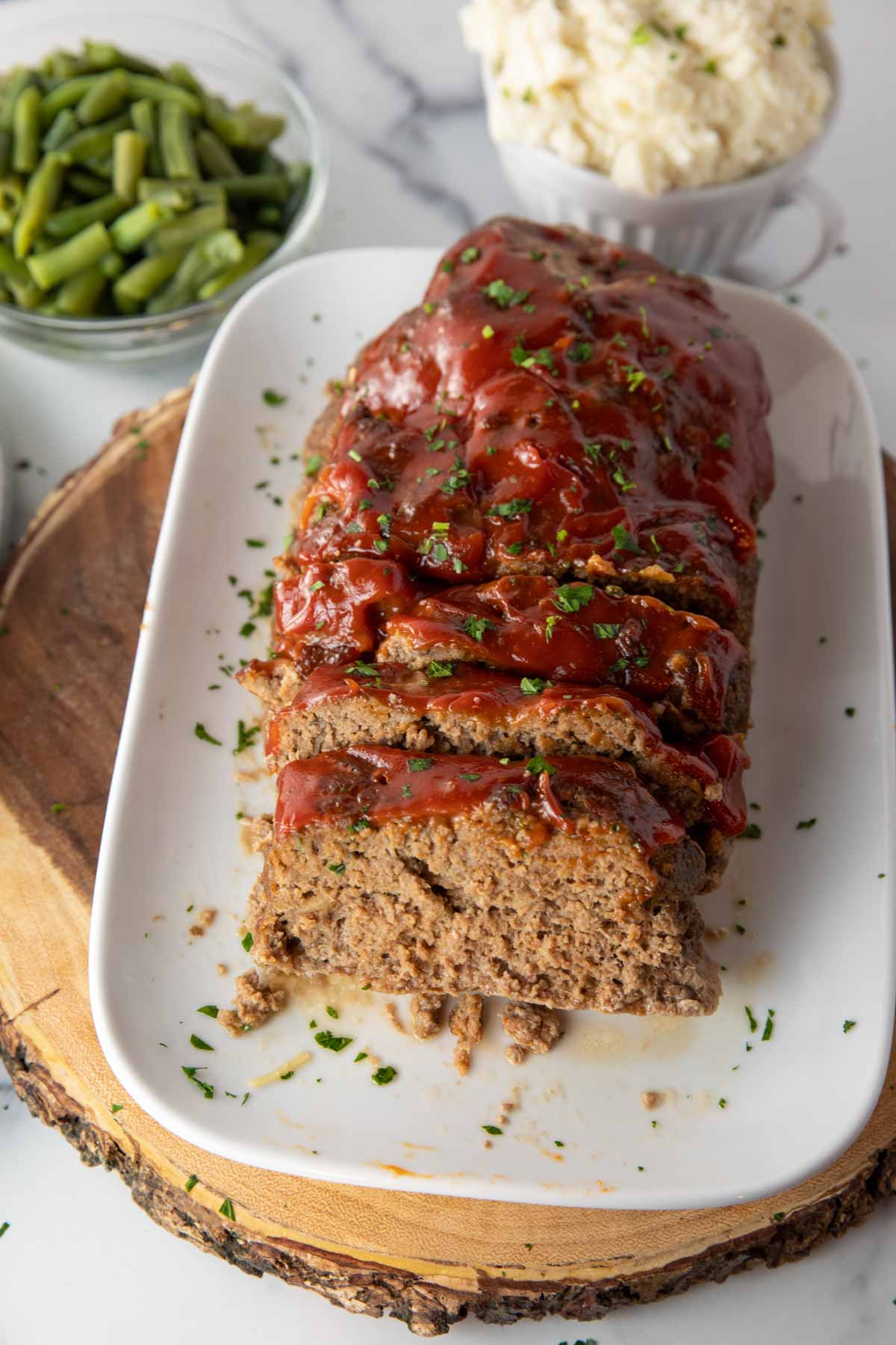 plate of lipton onion soup meatloaf. Bowls of mashed potatoes and green beans sitting in background