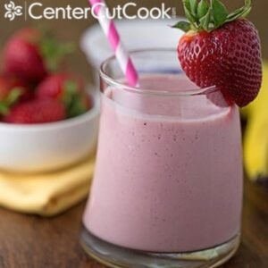 berry banana greek yogurt smoothie in a glass with a straw and garnished with a strawberry on the rim