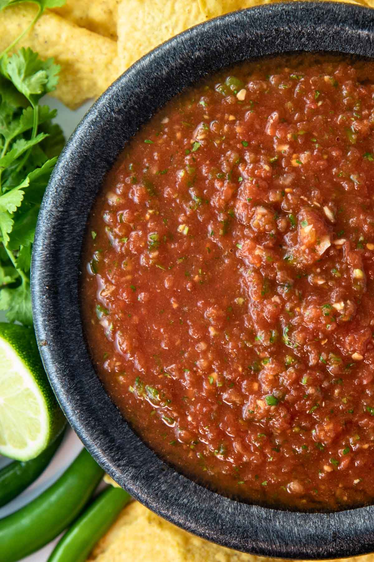 overhead of bowl of the best easy spicy salsa surrounded by tortilla chips, cilantro, limes, and peppers