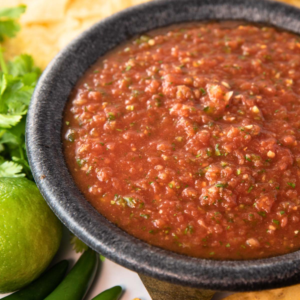 bowl of the best spicy salsa with chips, cilantro, lime, and peppers sitting beside.