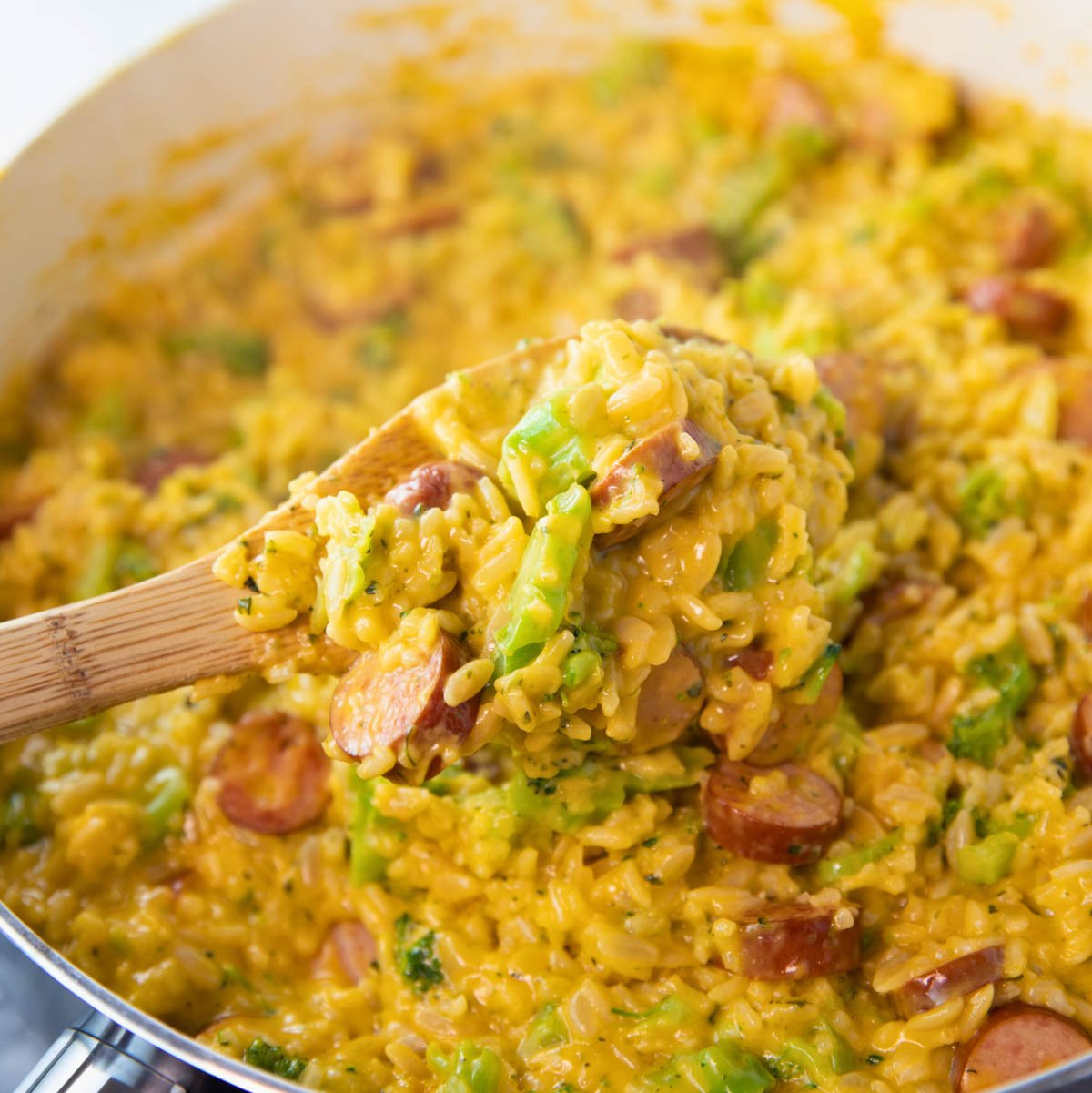 skillet of cheesy sausage and rice skillet with a wooden spoon stirring