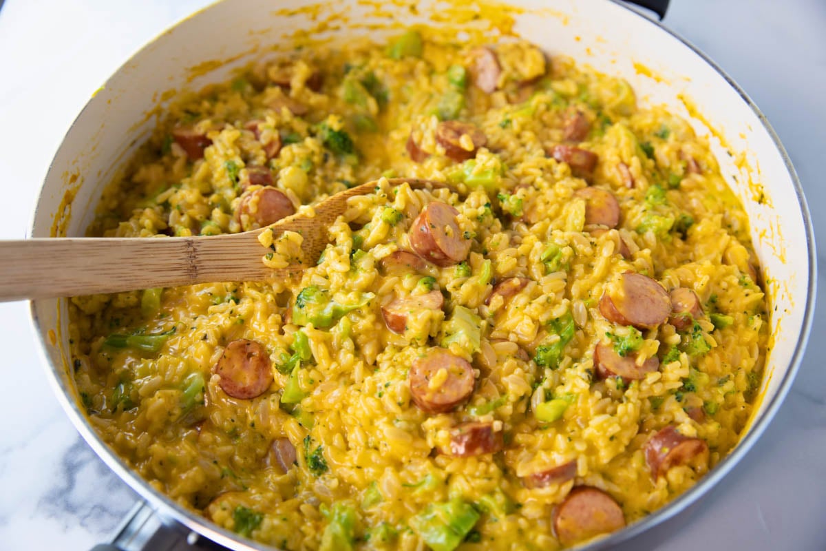 skillet of cheesy sausage and rice skillet with a wooden spoon for stirring
