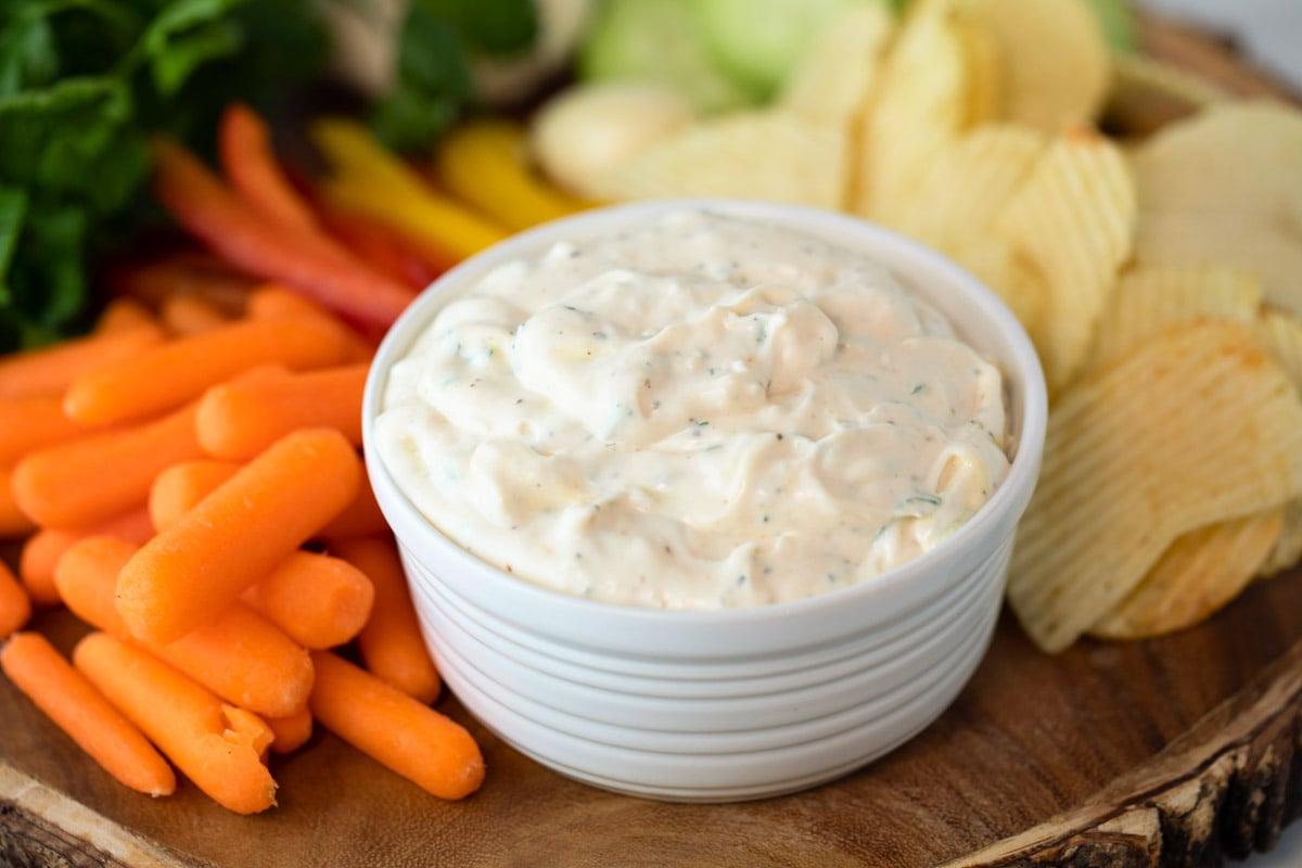 bowl of creamy garlic dip surrounded by fresh vegetables and chips for serving.