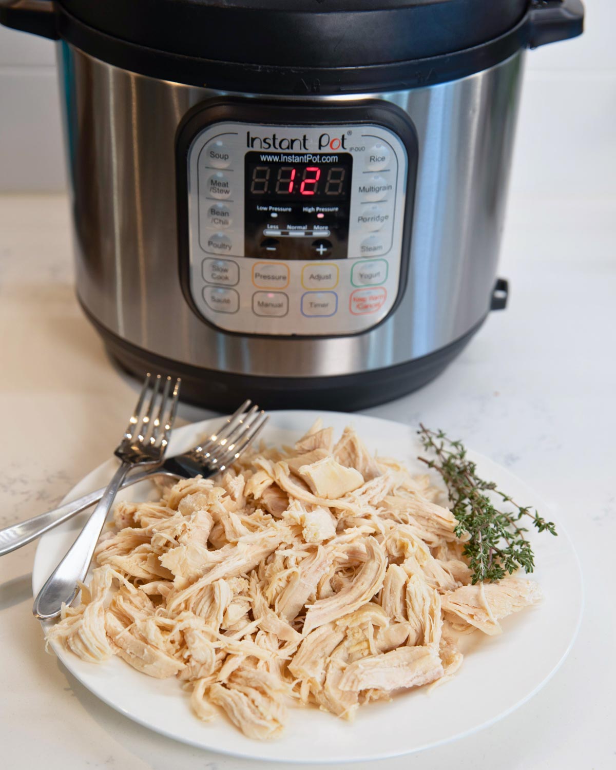 plate of easy instant pot shredded chicken with two forks, instant pot sitting in background.