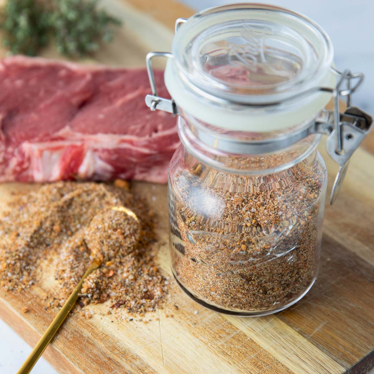 jar of easy steak seasoning with steak sitting in background on a wooden cutting board