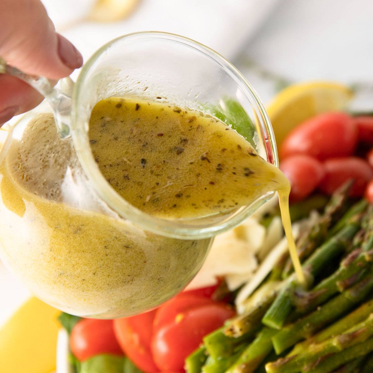 woman's hand pouring lemon vinaigrette over a grilled asparagus salad