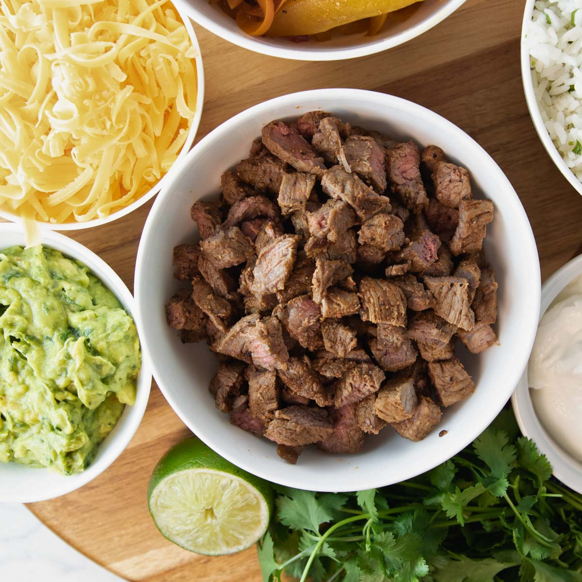 overhead of bowl of air fryer steak for fajitas surrounded by bowls of fajita and quesadilla toppings.