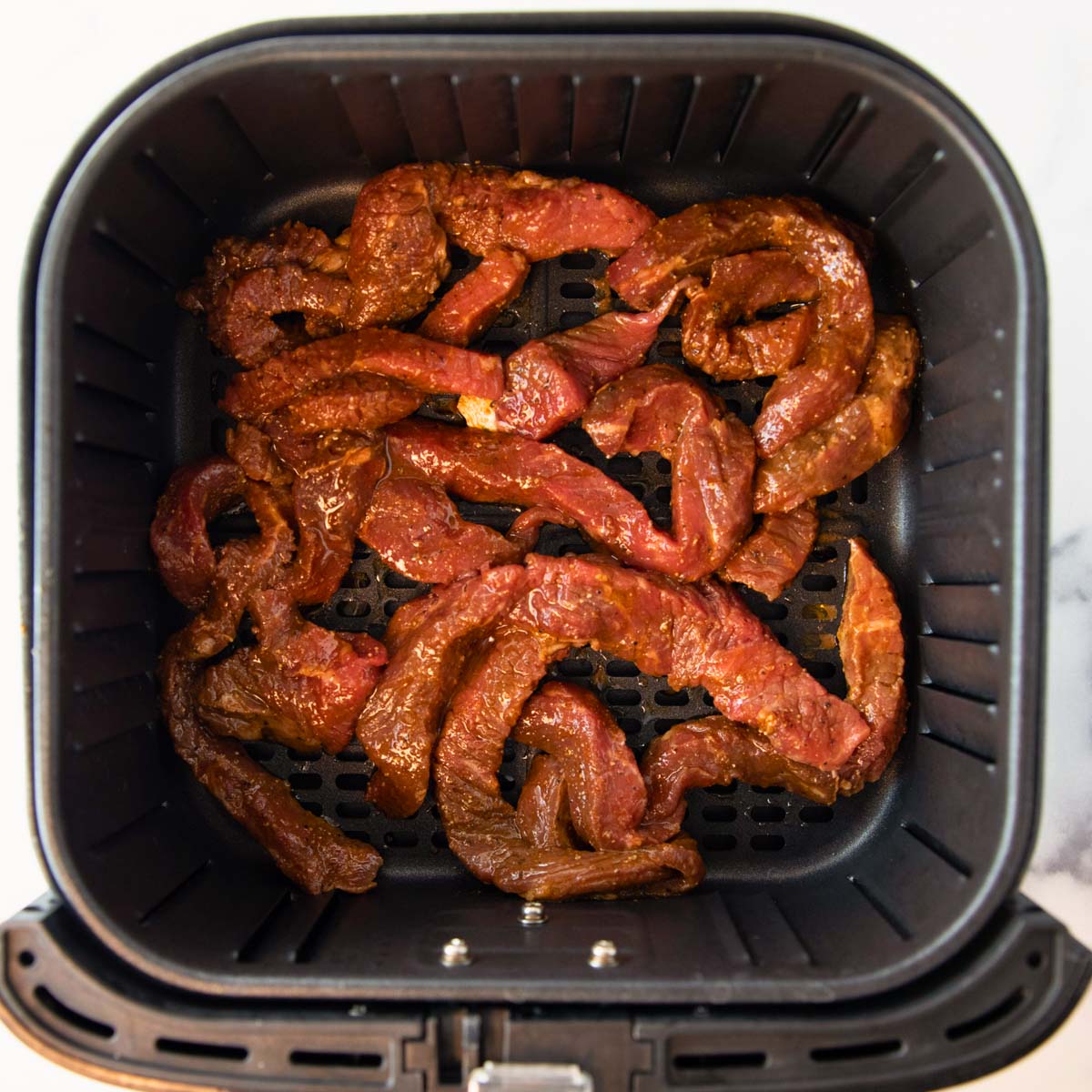 overhead of air fryer basket with steak for burritos and fajitas
