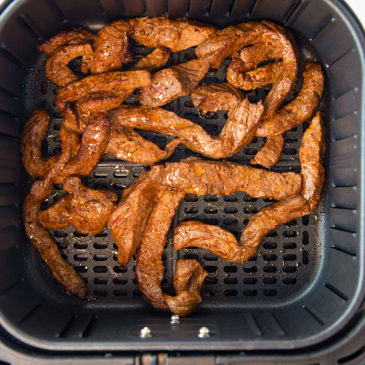 overhead of air fryer basket with strips of air fryer steak for burritos and fajitas