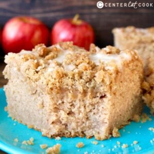 piece of apple cinnamon coffee cake on a plate. Fresh apples sitting in background.