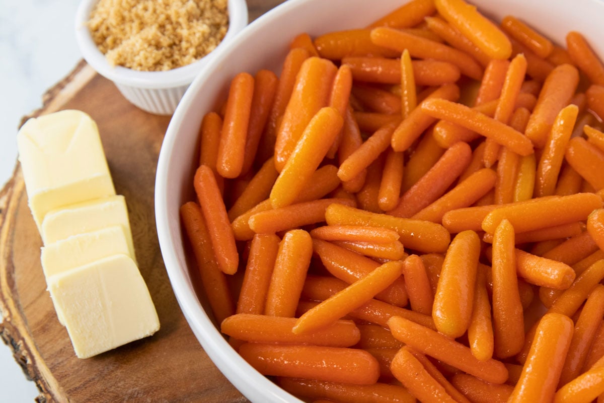 bowl of cooked carrots with butter and brown sugar sitting beside