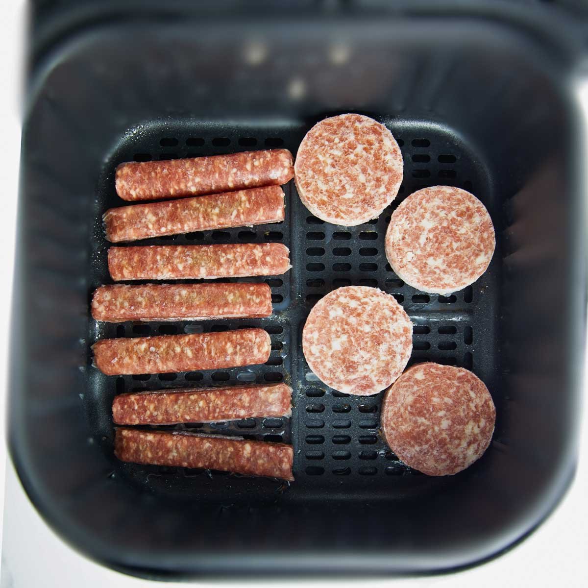 frozen breakfast sausage links and patties arranged in a single layer in the air fryer basket.