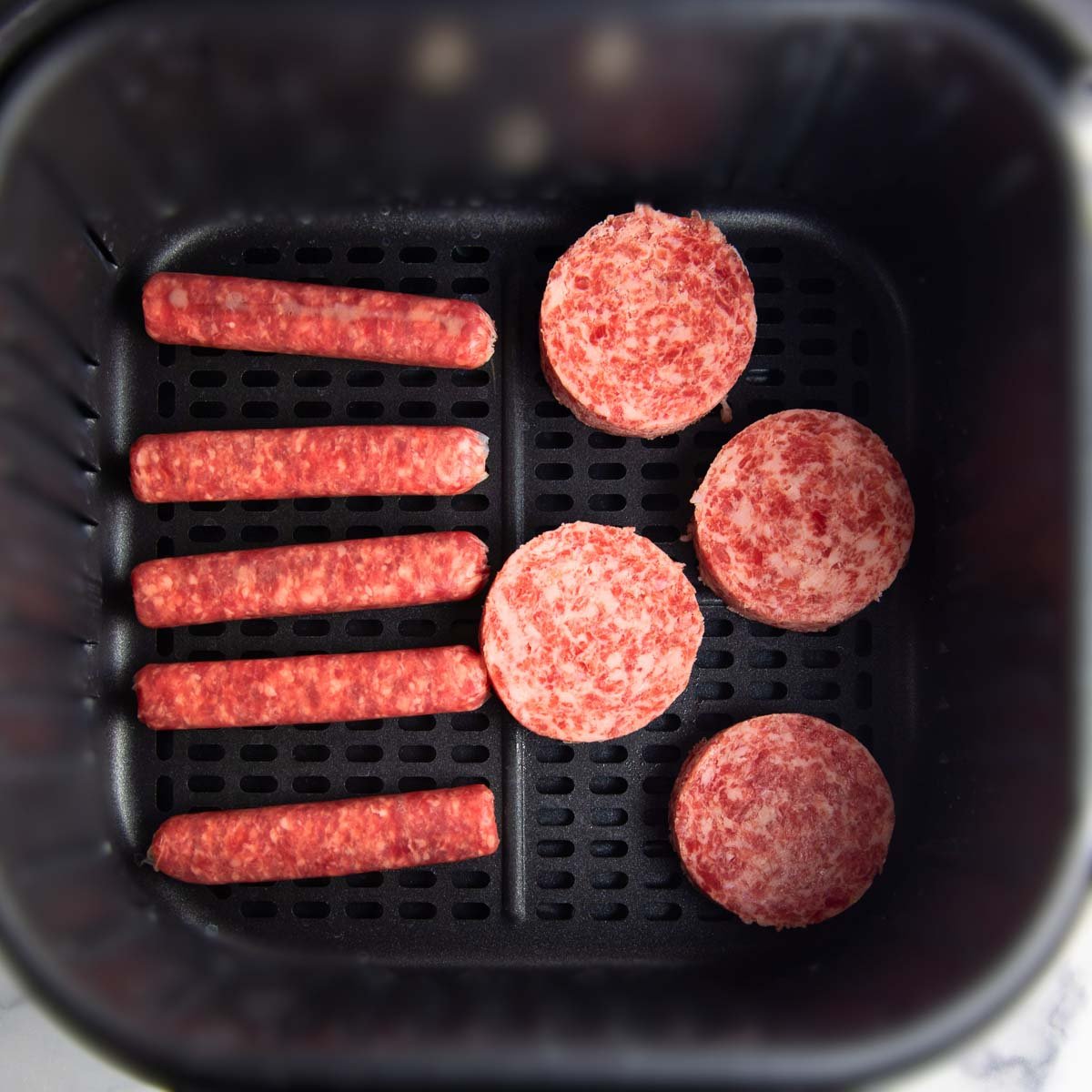 fresh breakfast sausage links and patties arranged in a single layer in the air fryer basket.