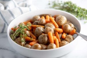 baby carrots and potatoes in a serving dish on a table alongside a roasted chicken dinner