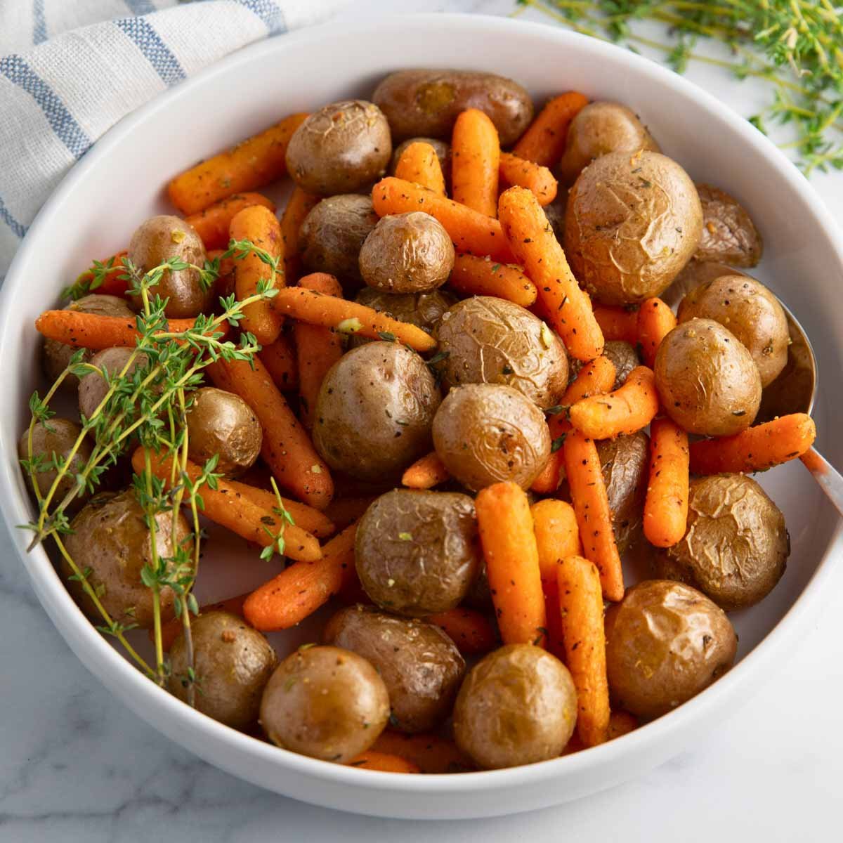 oven-roasted baby potatoes and carrots recipe seasoned with garlic, thyme, olive oil, salt and pepper, served in a bowl.