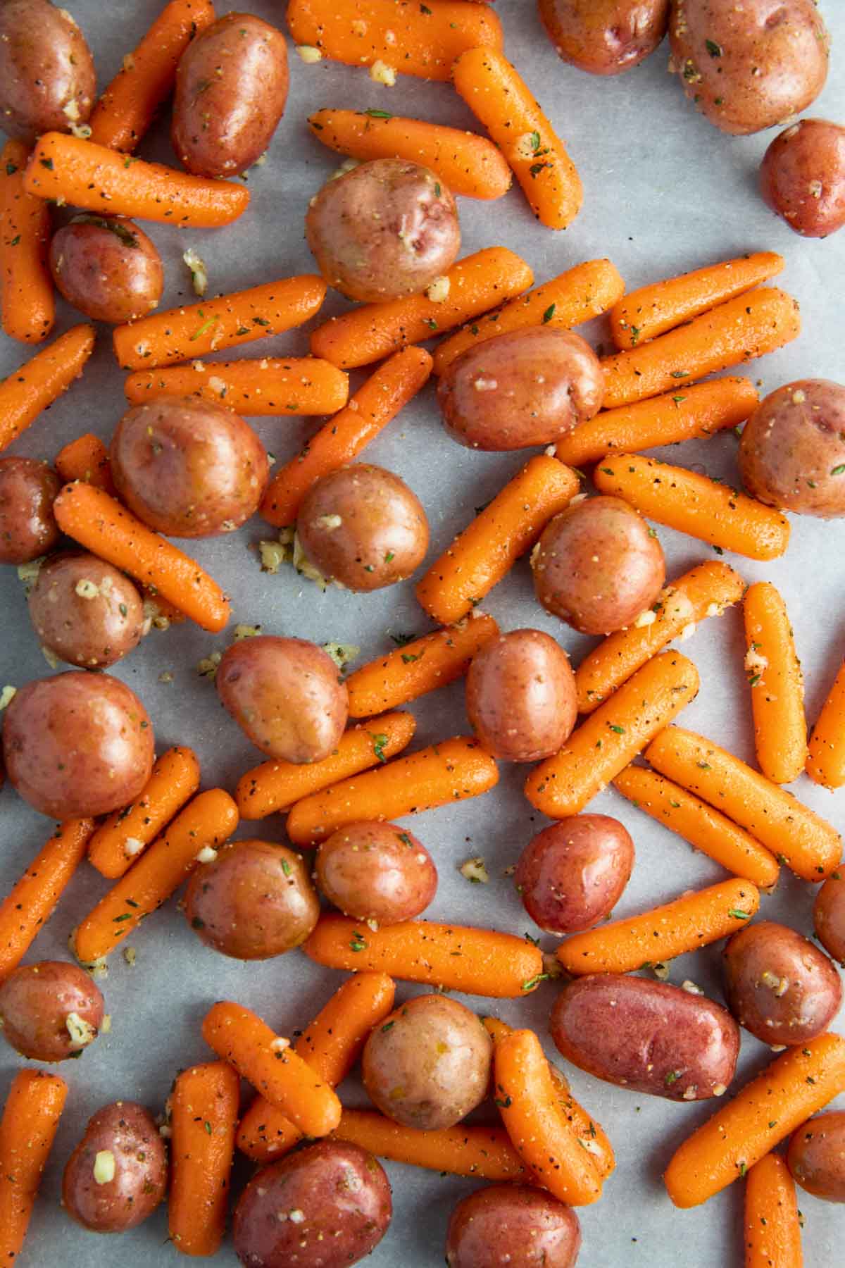 Baby potatoes and carrots tossed with olive oil, garlic, thyme and salt and pepper, evenly spread on a sheet pan lined with parchment paper, ready to roast.