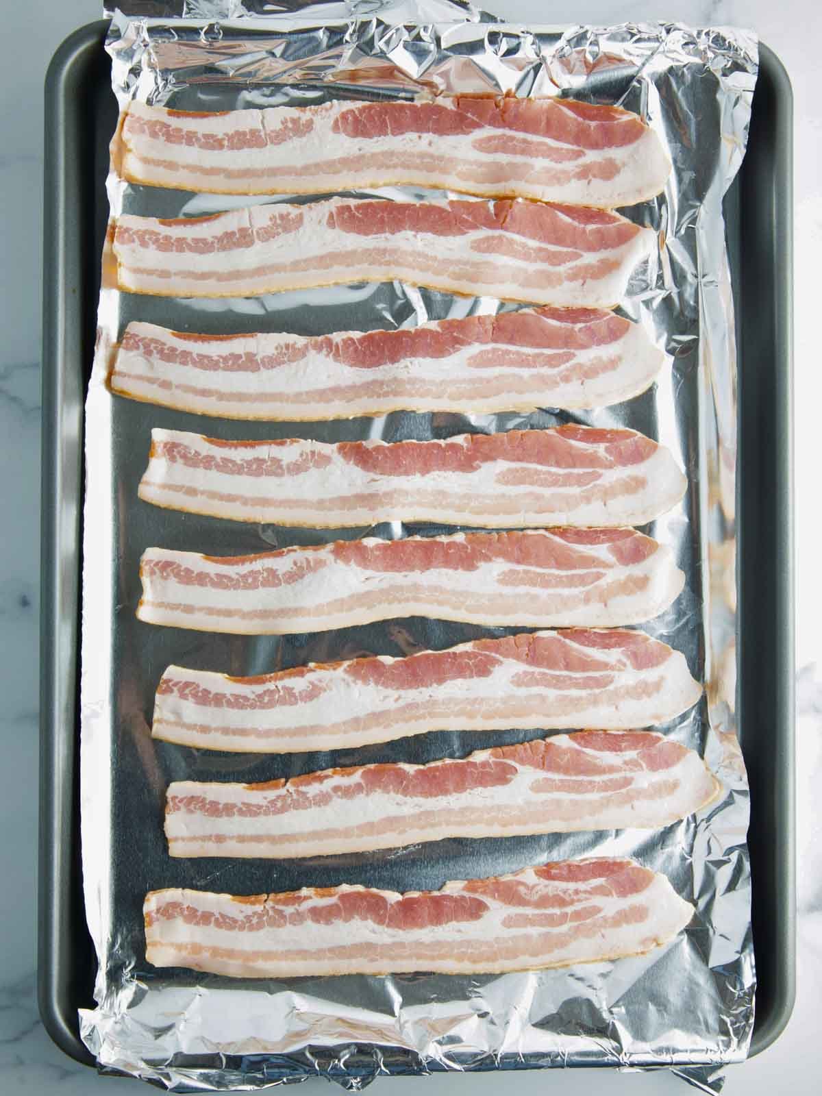 raw bacon strips evenly spaced on a parchment-lined baking sheet