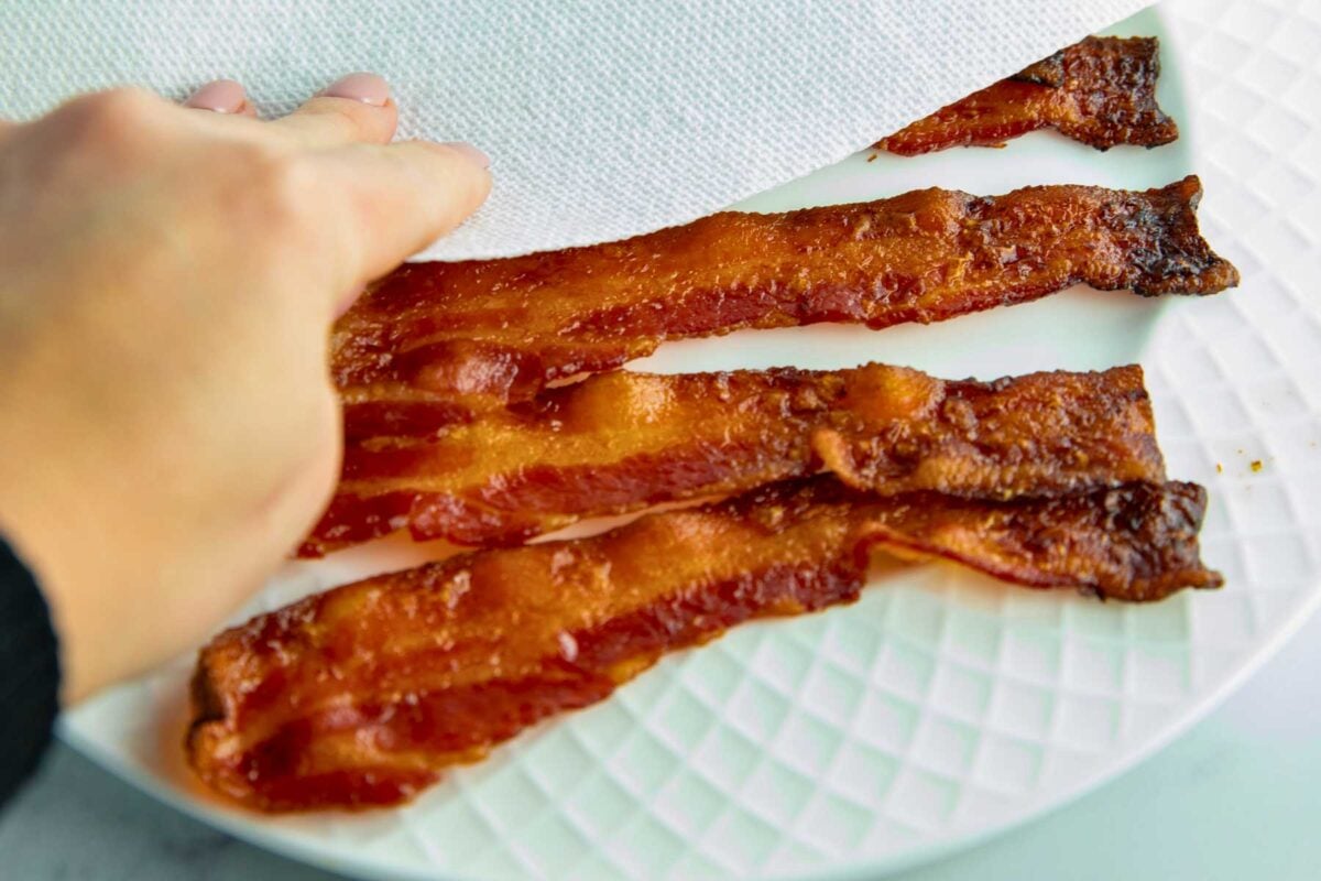 freshly baked bacon being transferred to a play lined with paper towels to drain excess grease.