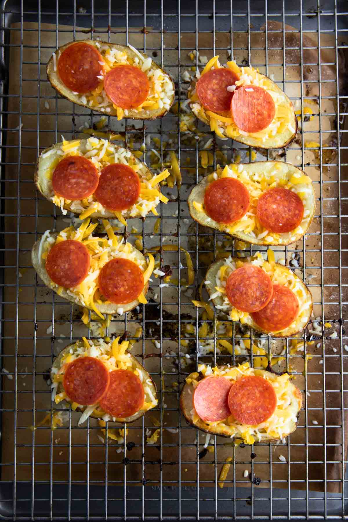 a closeup of potato skins arranged on a baking sheet with toppings added.