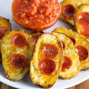 a plate of pizza potato skins with melted cheese, pepperoni, and Italian seasoning served with a side of pizza sauce.