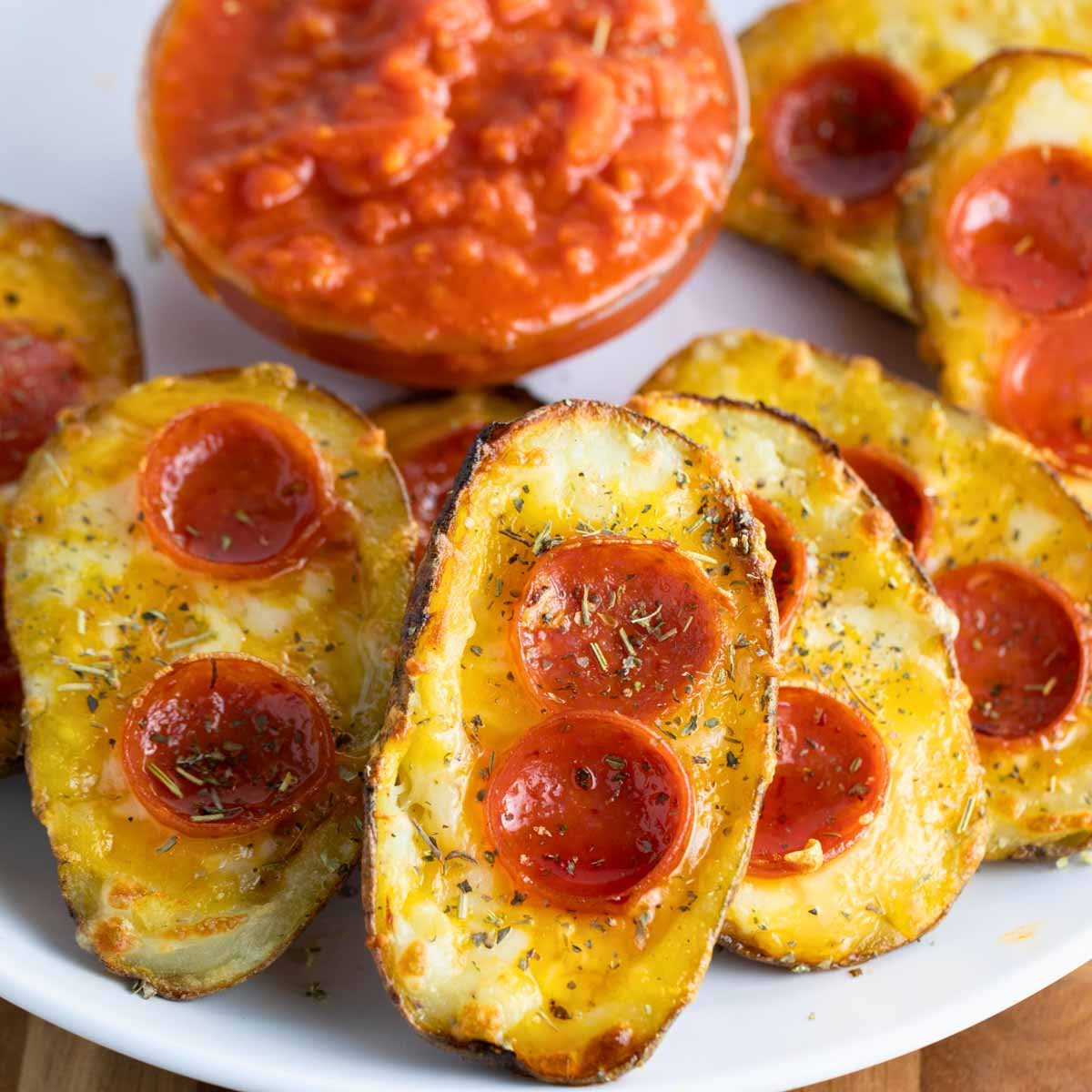 a plate of pizza potato skins with melted cheese, pepperoni, and Italian seasoning served with a side of marinara sauce.