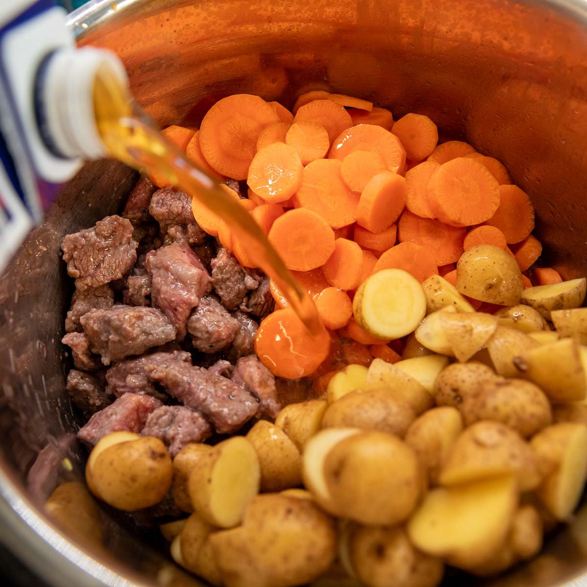 adding beef broth, potatoes and carrots to the Instant Pot.