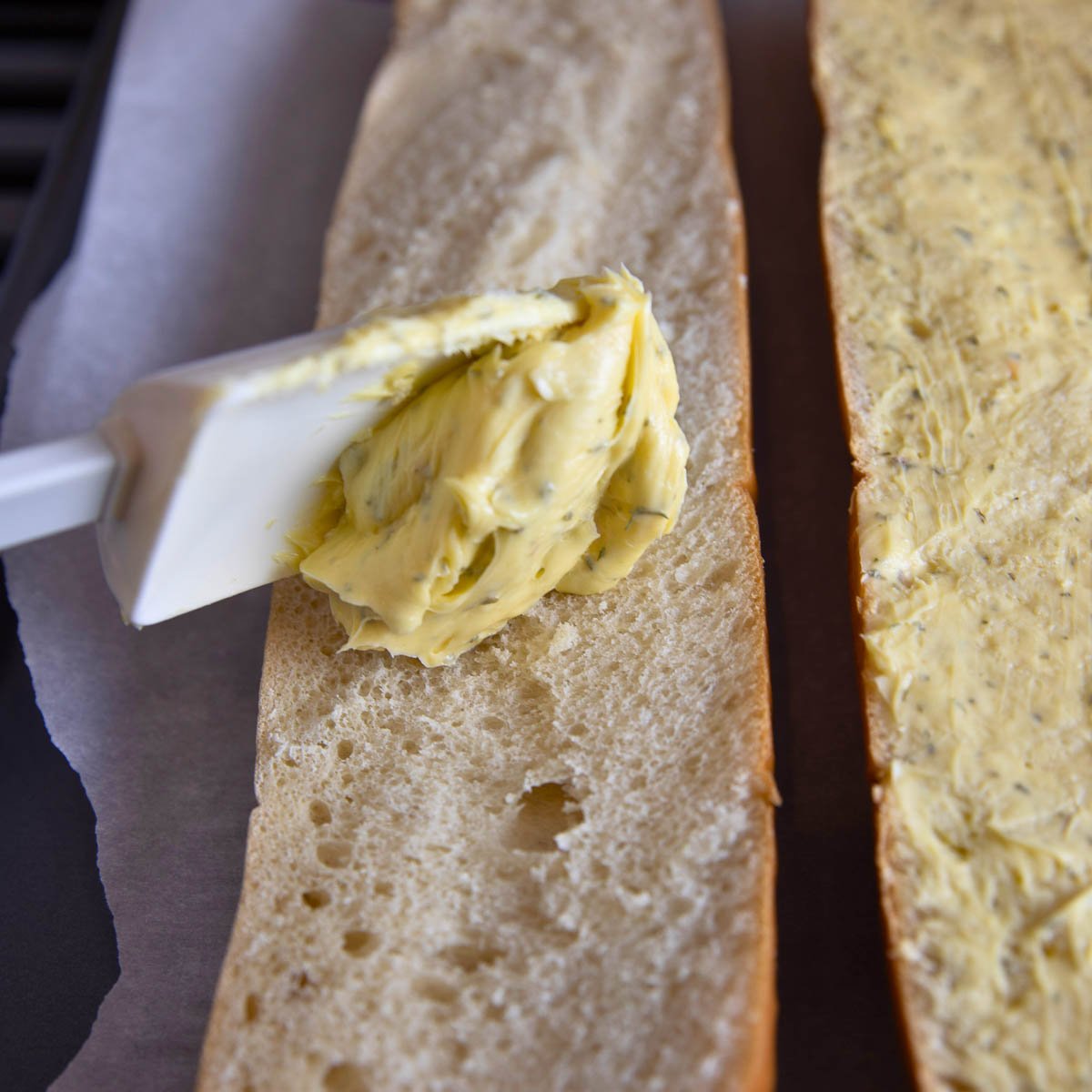 French bread loaf being slathered with garlic butter spread.